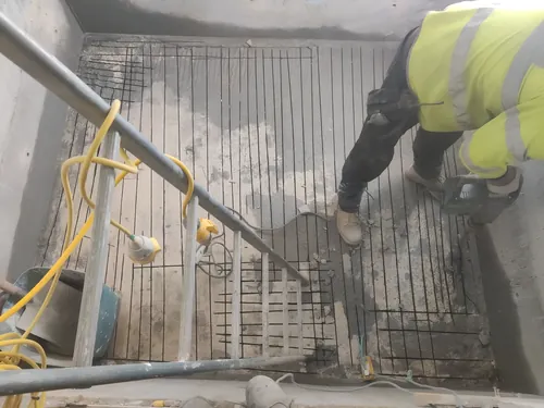 Top of a slab broken out down to the steel mesh, with an operator working in the recess.