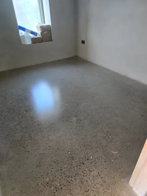 Polished concrete floor with exposed aggregate in a corner room, reflecting the window.