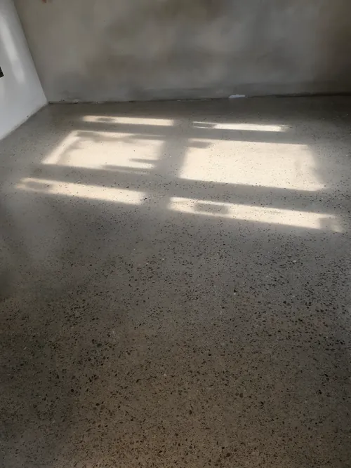 Polished concrete floor with the aggregate exposed, in a room with plastered walls.