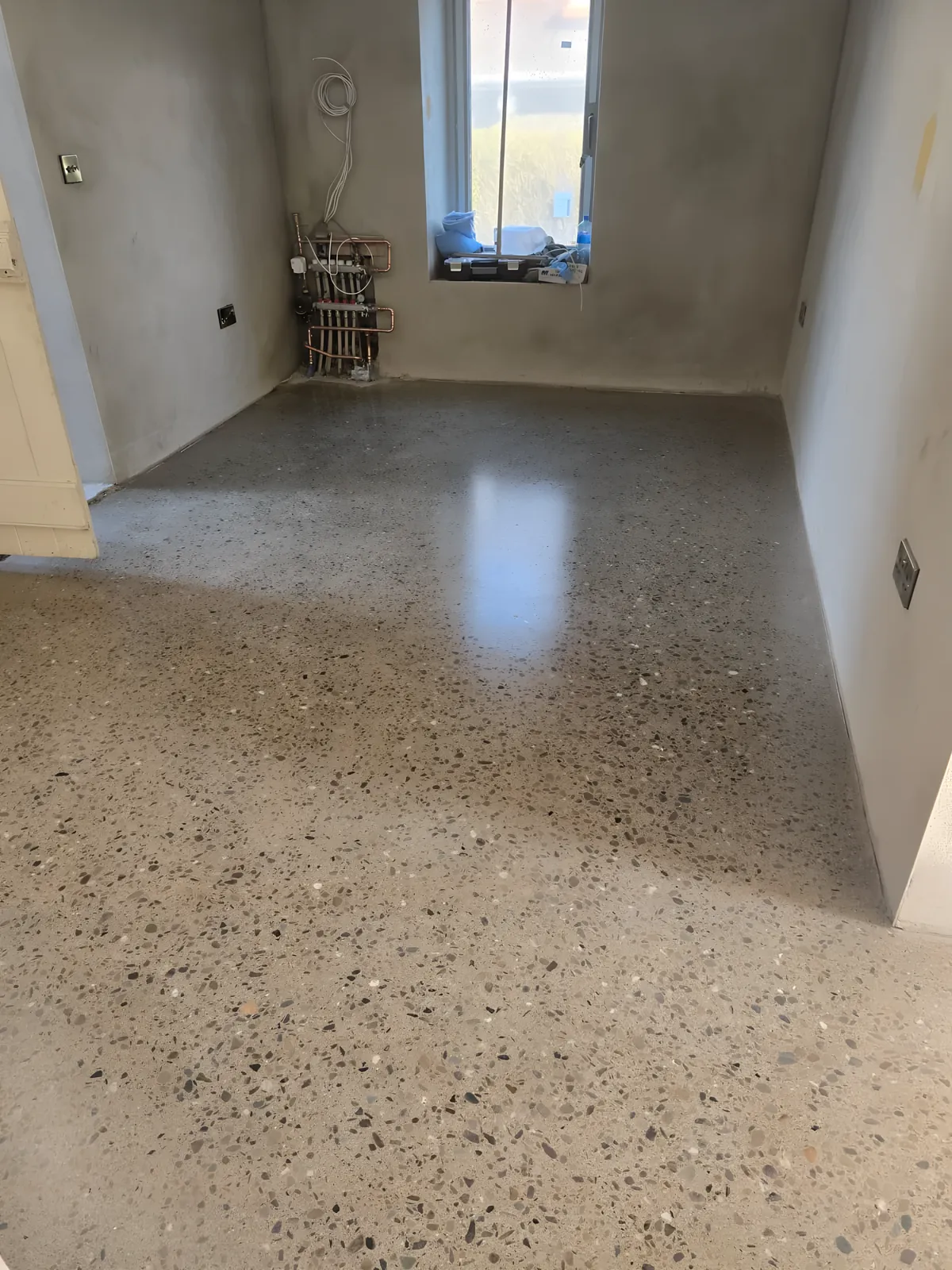 Polished concrete floor in a ground-floor room, the sheen catching the light from the window.