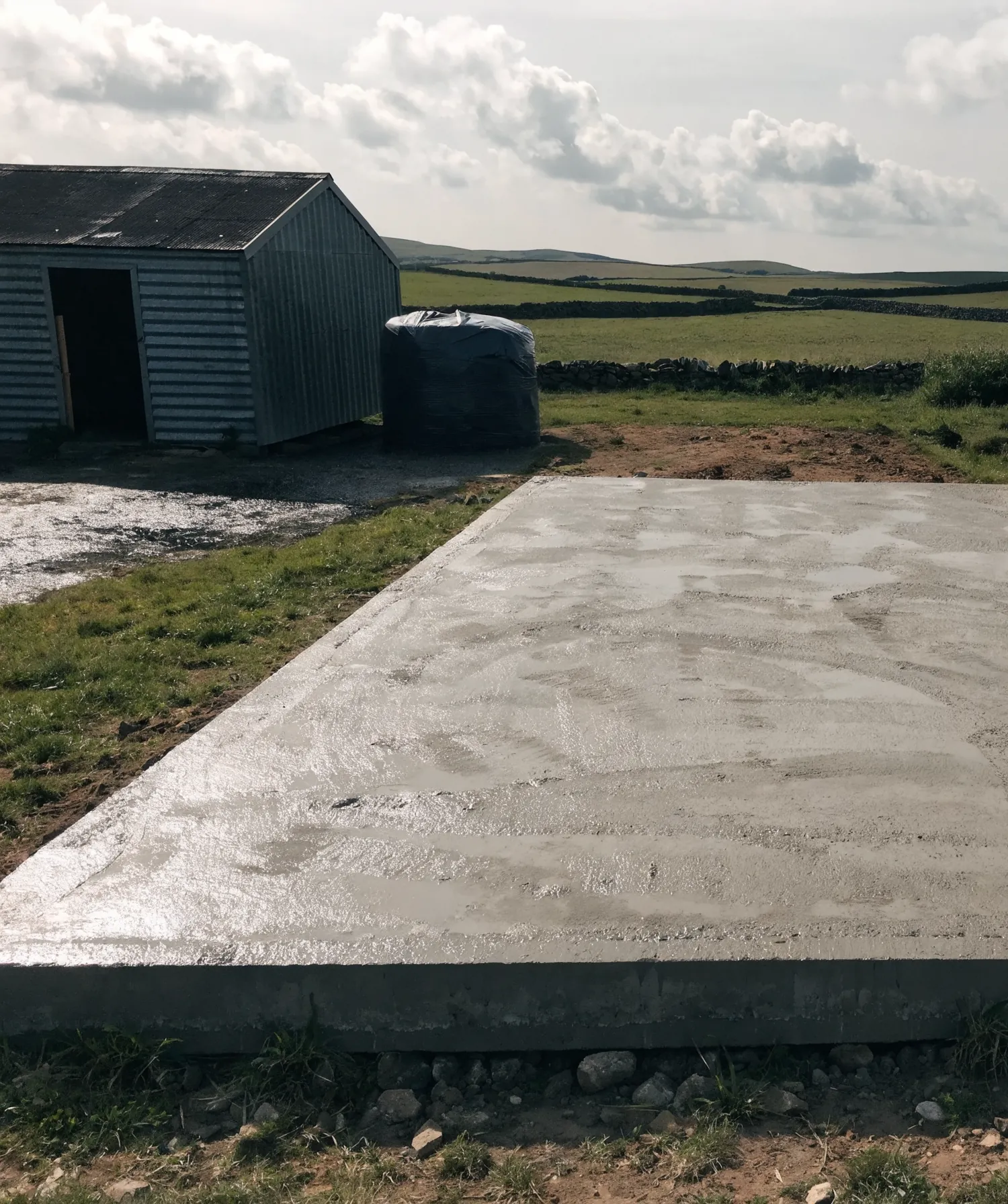 Freshly poured concrete slab for a farm shed beside a farmyard.