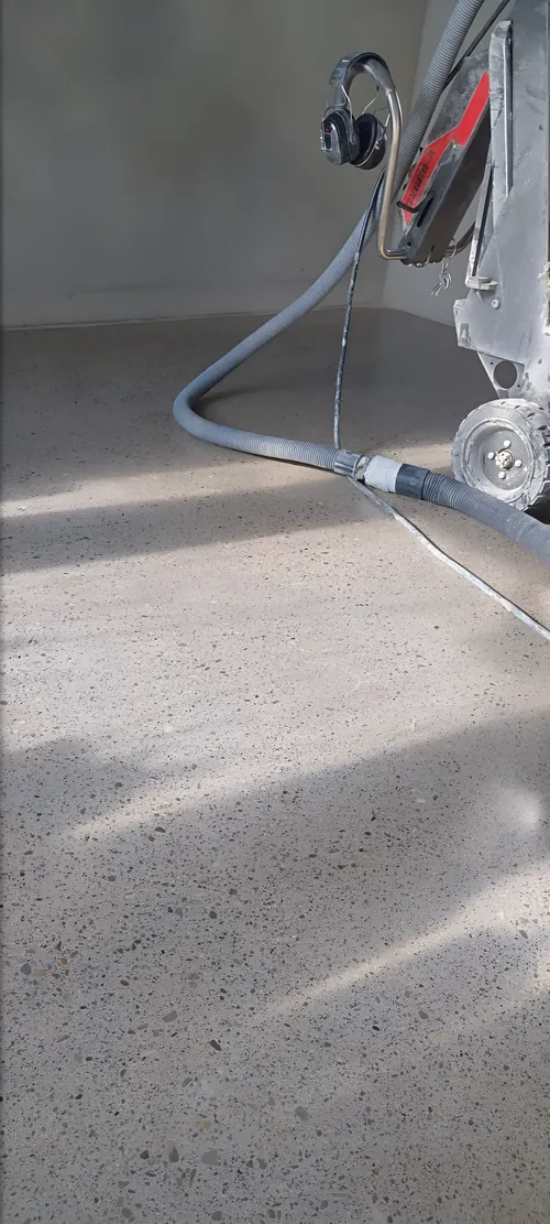 Floor grinder at work on a concrete floor, with its dust extraction hose.
