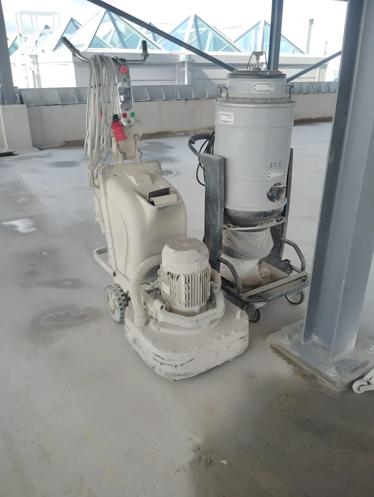 Floor grinder and dust extractor on a concrete slab in a building under construction.