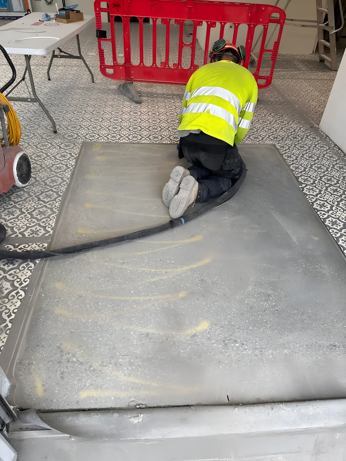 Operator grinding a patch of concrete floor inside a tiled room, with the dust hose attached.