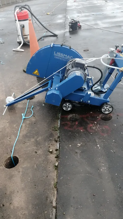Walk-behind floor saw cutting a concrete slab, water-fed, beside a cored hole.