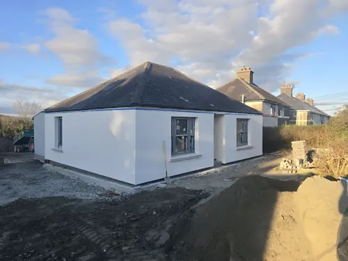 Newly rendered bungalow with a hipped slate roof, the site still to be landscaped.