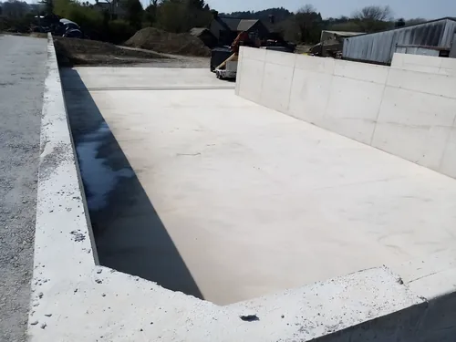 Cast concrete wall along the edge of a new concrete floor, with the shuttering struck.