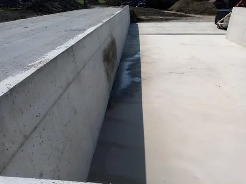 Tall cast concrete wall and floor of a new pit, with the shuttering struck.