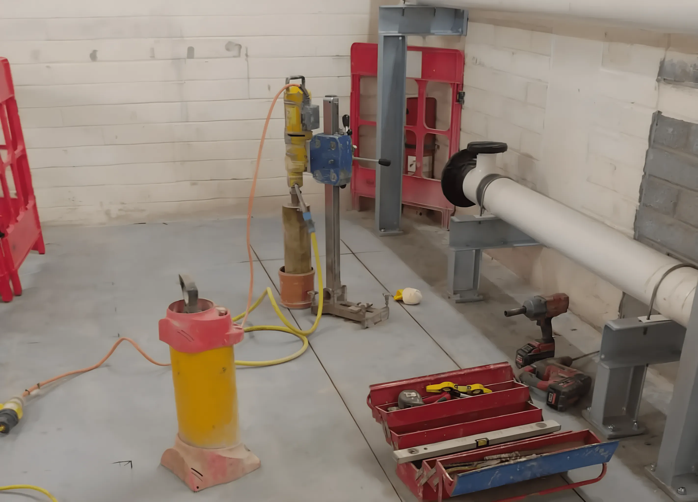 Core drill on its stand in a plant room, beside a pipe run through the block wall.