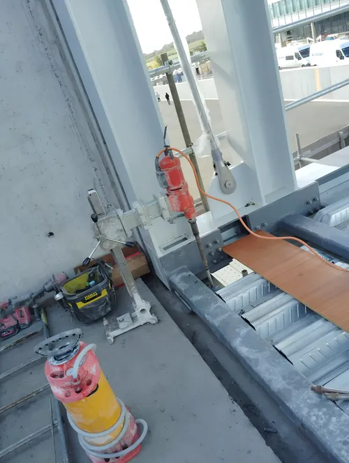 Rig-mounted core drill set up beside the steel frame of a building, with spare bits on the deck.