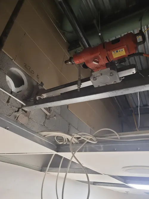Core drill on a rail, coring a round opening through a block wall at ceiling height.
