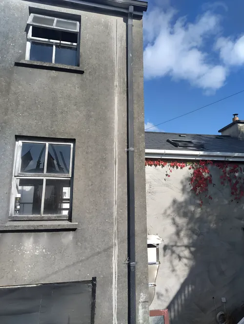 Full-height saw cut in a rendered wall, running beside the downpipe.
