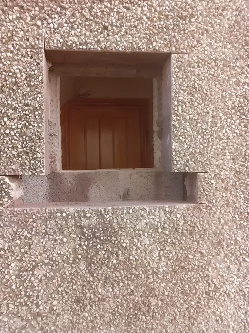 Square opening cut through a pebble-dashed wall.