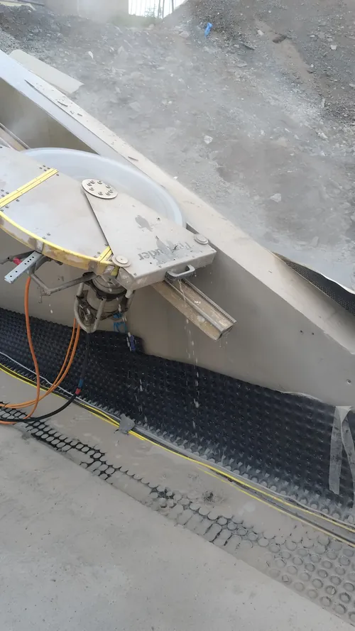 Track-mounted saw cutting along a sloped concrete face, water-fed.