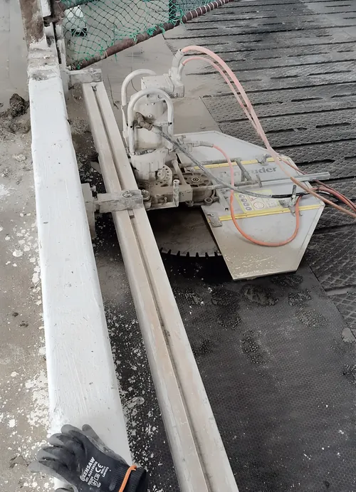 Track-mounted wall saw set up along a concrete edge, with the water feed connected.