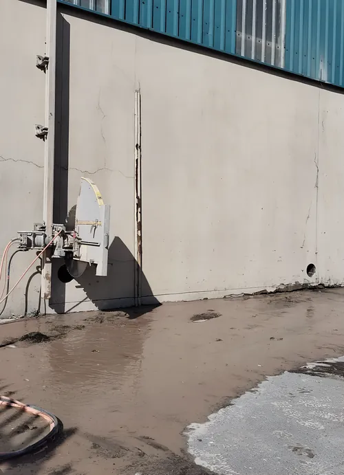 Wall saw mounted on a concrete wall, with a vertical cut made.