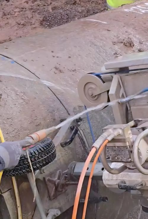 Diamond wire running round the pulleys as it cuts through a concrete pipe, water-fed.